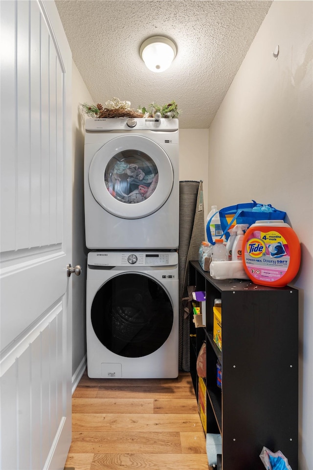 clothes washing area featuring stacked washer and clothes dryer, a textured ceiling, and light hardwood / wood-style floors