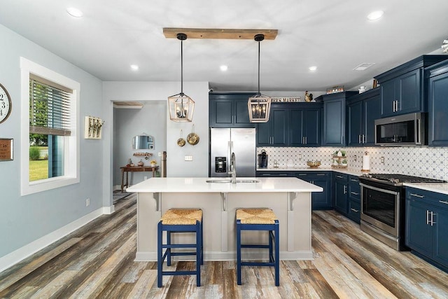 kitchen featuring a kitchen bar, appliances with stainless steel finishes, blue cabinets, and a center island with sink