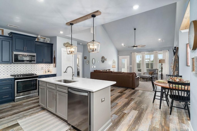 kitchen featuring ceiling fan, appliances with stainless steel finishes, decorative backsplash, a kitchen island with sink, and sink