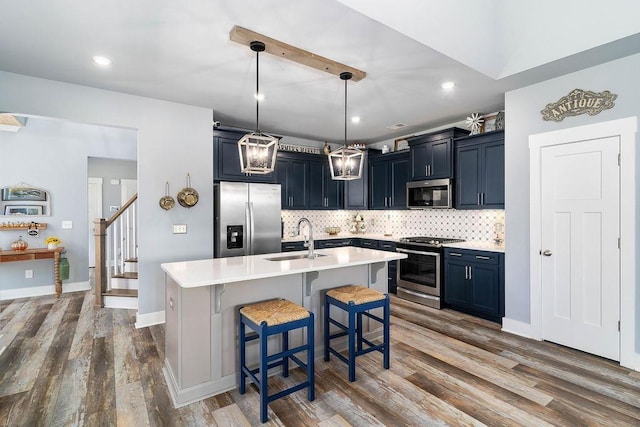 kitchen featuring a center island with sink, appliances with stainless steel finishes, hanging light fixtures, a breakfast bar, and sink