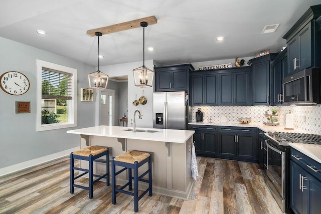 kitchen featuring decorative light fixtures, sink, stainless steel appliances, and an island with sink