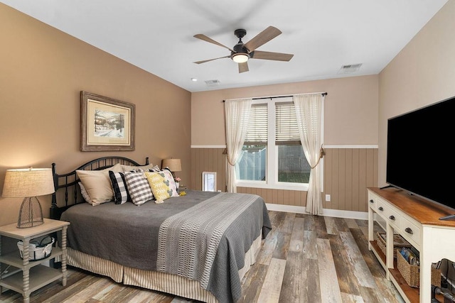 bedroom with ceiling fan, hardwood / wood-style floors, and wooden walls