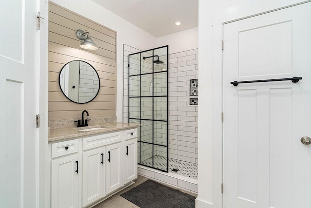 bathroom featuring vanity, tile patterned floors, wood walls, and a tile shower