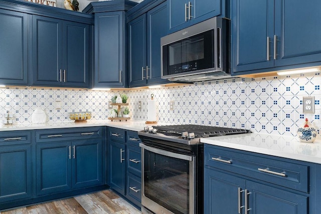 kitchen with hardwood / wood-style floors, appliances with stainless steel finishes, blue cabinets, and tasteful backsplash