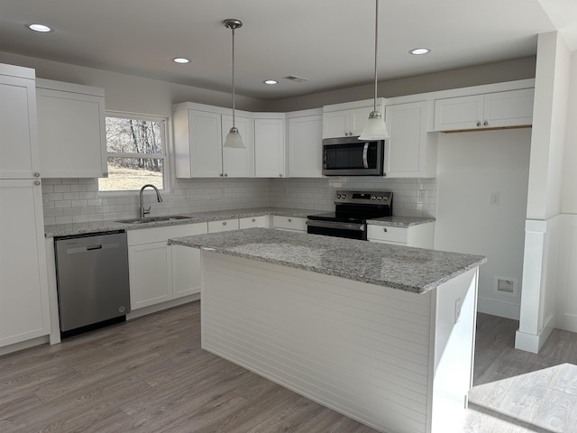 kitchen featuring light stone countertops, pendant lighting, white cabinets, a center island, and stainless steel appliances