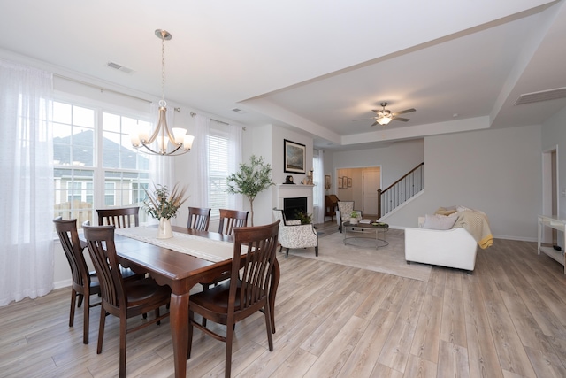 dining room featuring light wood-type flooring, ceiling fan with notable chandelier, and a tray ceiling