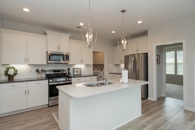 kitchen with white cabinetry, stainless steel appliances, a kitchen island with sink, decorative light fixtures, and sink