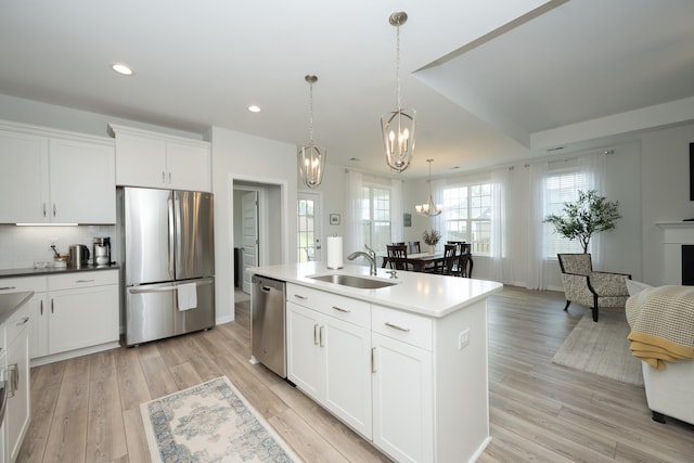 kitchen featuring white cabinets, stainless steel appliances, an island with sink, sink, and hanging light fixtures