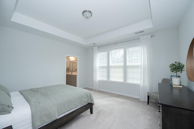 bedroom with ensuite bath, light carpet, and a tray ceiling