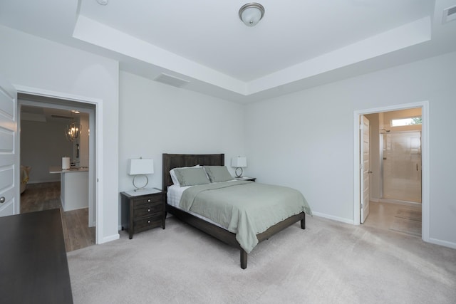 carpeted bedroom featuring ensuite bathroom and a tray ceiling