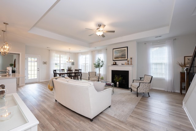 living room with ceiling fan, light wood-type flooring, and a tray ceiling