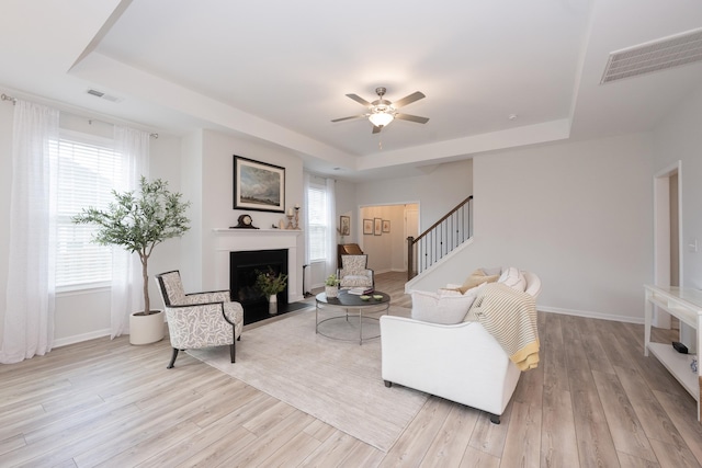 living room featuring light hardwood / wood-style floors, a tray ceiling, and a healthy amount of sunlight