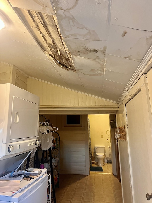 laundry room featuring stacked washer and clothes dryer and wood walls