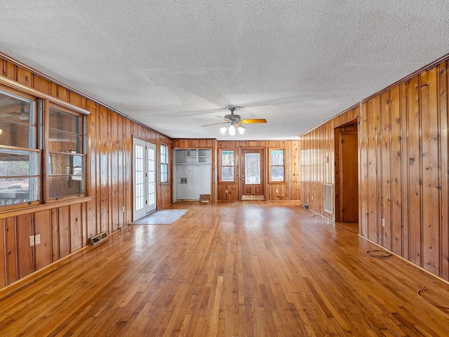 unfurnished living room with ceiling fan, french doors, and wooden walls