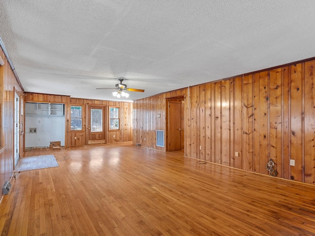 unfurnished living room featuring ceiling fan, a textured ceiling, light hardwood / wood-style flooring, and wood walls