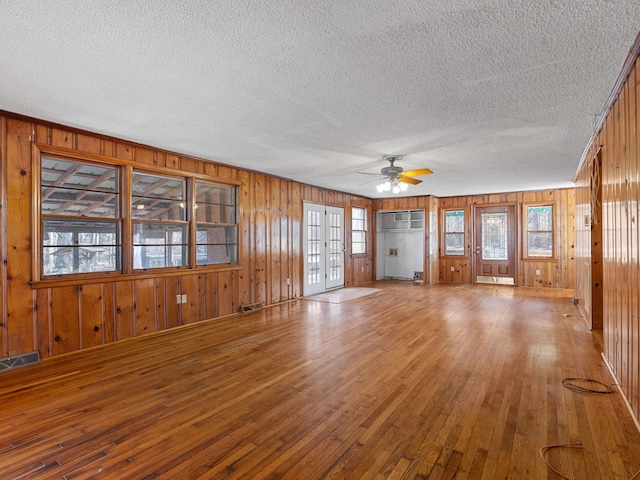 unfurnished living room with ceiling fan, a wall mounted AC, wood-type flooring, and a textured ceiling