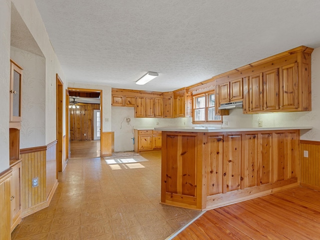 kitchen featuring a textured ceiling, kitchen peninsula, and wooden walls