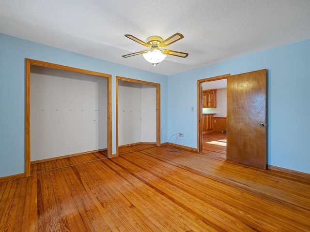 unfurnished bedroom with ceiling fan, two closets, a textured ceiling, and hardwood / wood-style floors