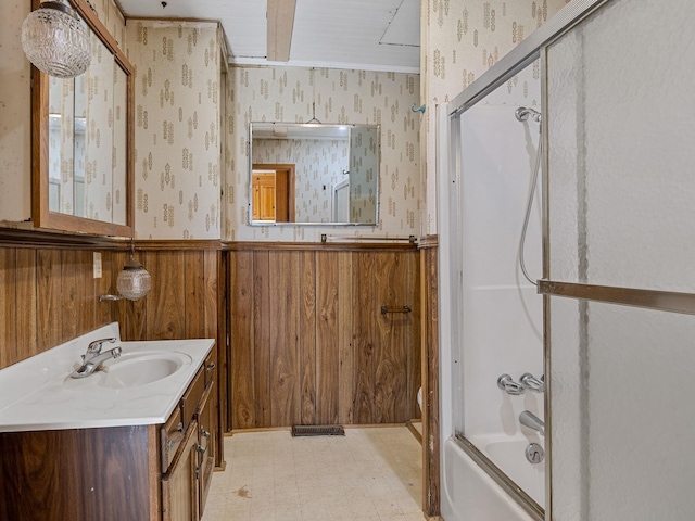 bathroom featuring wooden walls, combined bath / shower with glass door, and vanity