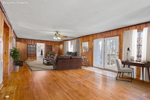 living room featuring ceiling fan, light wood-type flooring, wooden walls, and a textured ceiling