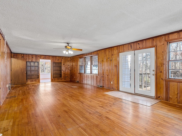 unfurnished living room with ceiling fan, wood walls, a textured ceiling, and light hardwood / wood-style flooring