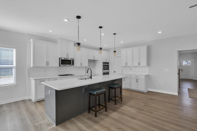 kitchen with white gas stovetop, decorative light fixtures, white cabinetry, sink, and a kitchen island with sink