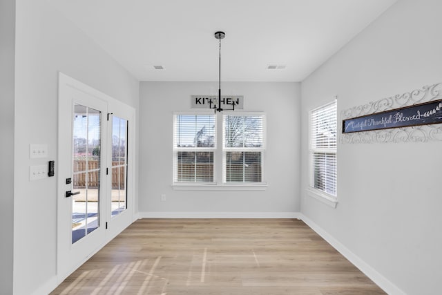 unfurnished dining area with plenty of natural light, a notable chandelier, and light wood-type flooring