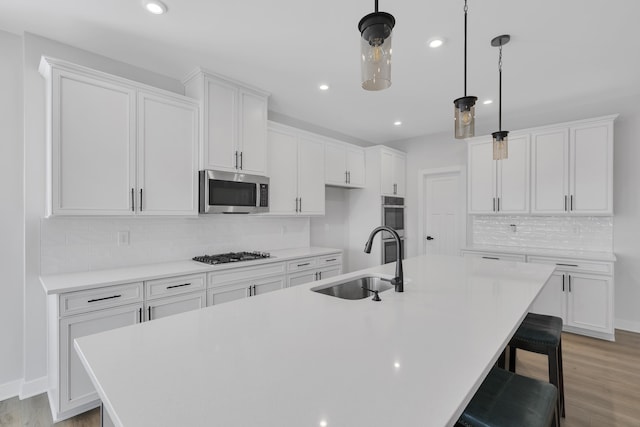 kitchen with an island with sink, sink, stainless steel appliances, and white cabinetry