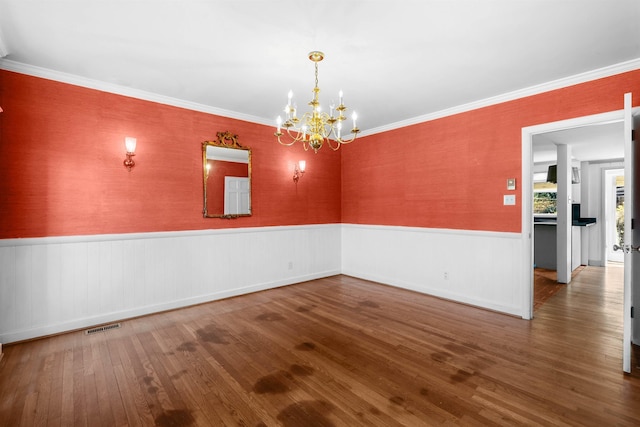 unfurnished room featuring wood-type flooring, ornamental molding, and a notable chandelier