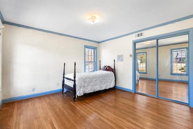 bedroom featuring a closet, ornamental molding, wood-type flooring, and multiple windows