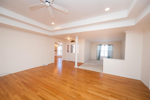 unfurnished living room with ceiling fan, ornate columns, light hardwood / wood-style floors, and a tray ceiling