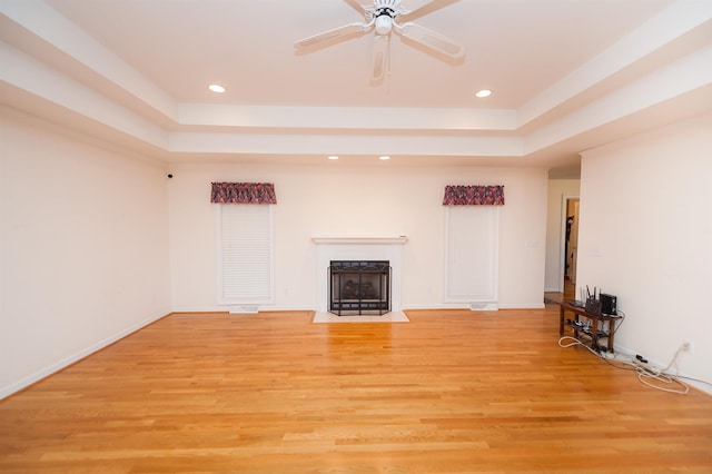 unfurnished living room with ceiling fan, a raised ceiling, and light hardwood / wood-style flooring