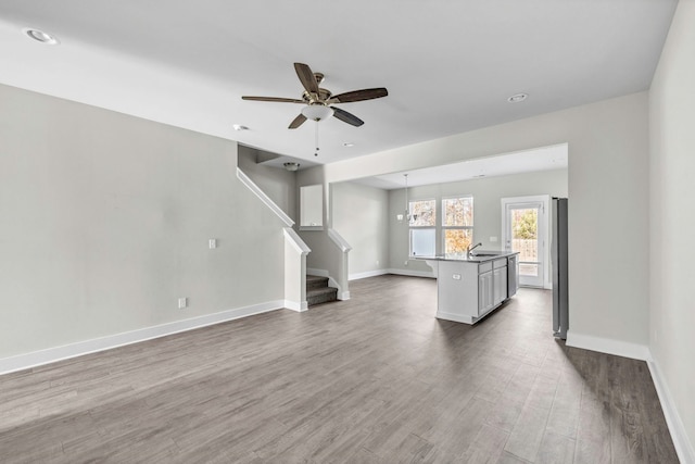 unfurnished living room with ceiling fan with notable chandelier, sink, and hardwood / wood-style flooring