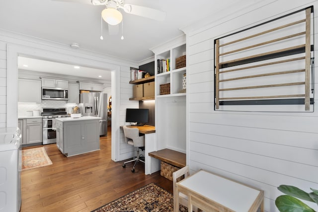 interior space with a center island, decorative backsplash, crown molding, appliances with stainless steel finishes, and dark hardwood / wood-style flooring