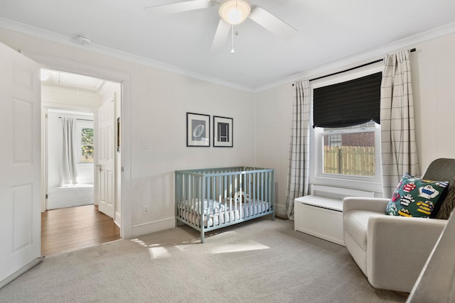 bedroom with ceiling fan, light colored carpet, a nursery area, and ornamental molding