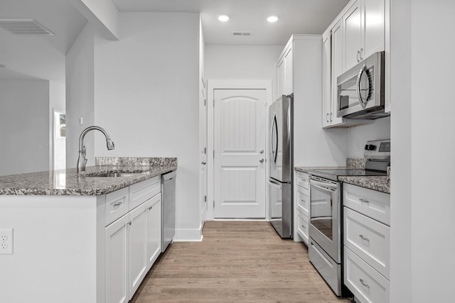 kitchen with appliances with stainless steel finishes, white cabinetry, sink, light wood-type flooring, and stone counters