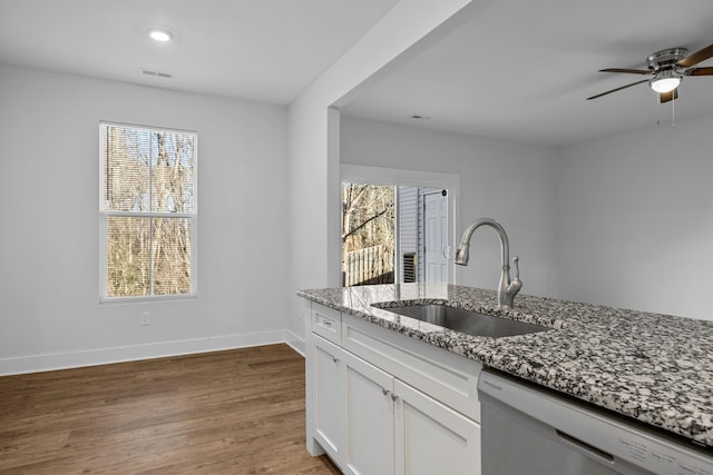 kitchen with white cabinets, dishwasher, sink, hardwood / wood-style flooring, and light stone counters