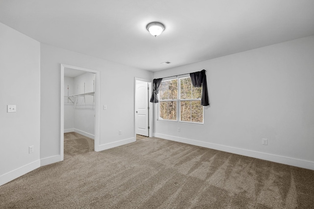 unfurnished bedroom featuring a closet, a walk in closet, and carpet floors