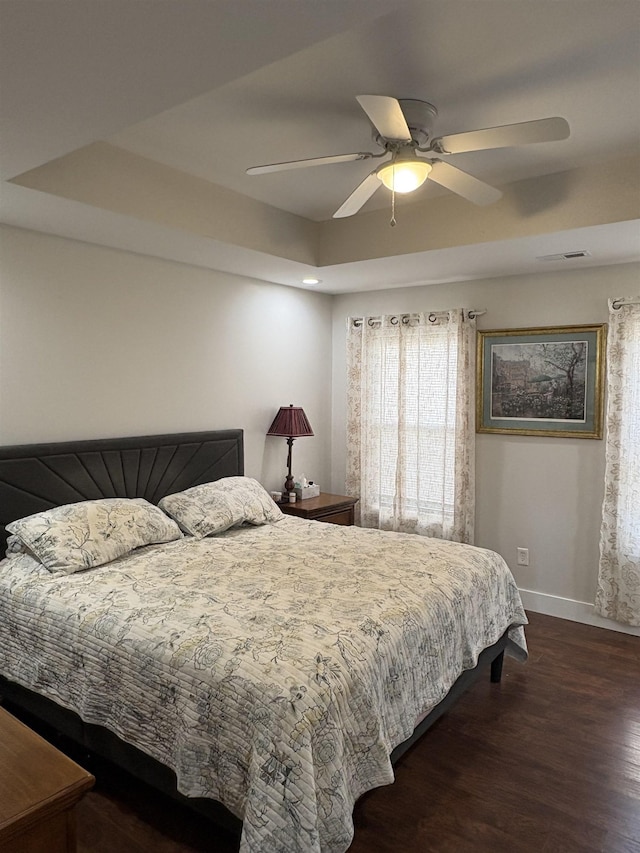 bedroom with ceiling fan, dark wood-type flooring, and a raised ceiling