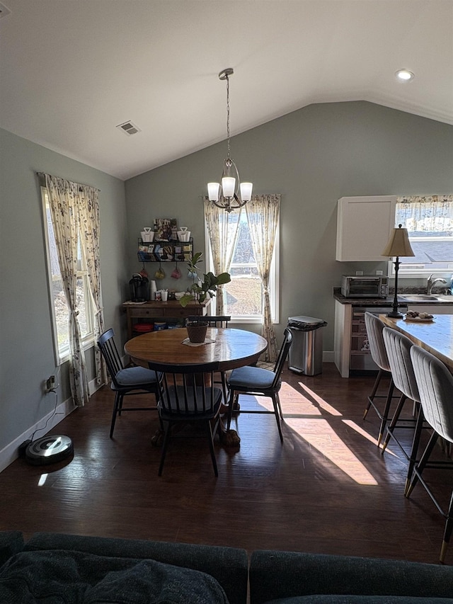 dining area with dark wood-type flooring, a chandelier, and vaulted ceiling