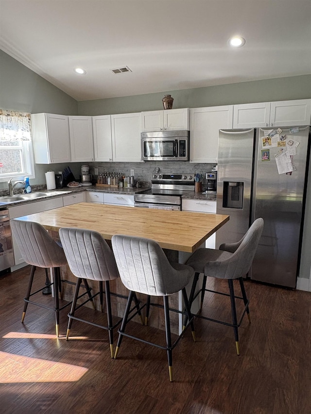 kitchen with white cabinets, butcher block countertops, appliances with stainless steel finishes, and a breakfast bar