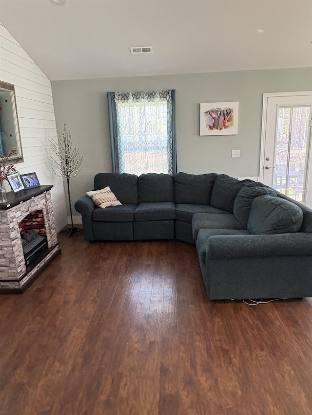 living room featuring dark wood-type flooring, vaulted ceiling, a stone fireplace, and a healthy amount of sunlight