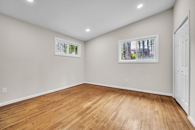 unfurnished room featuring lofted ceiling, plenty of natural light, and light hardwood / wood-style flooring