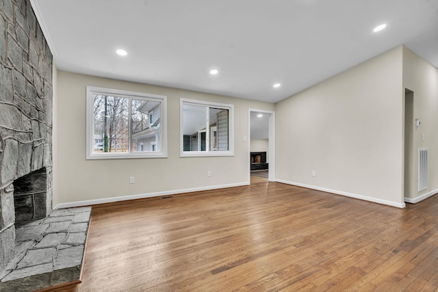 unfurnished living room with wood-type flooring and a stone fireplace