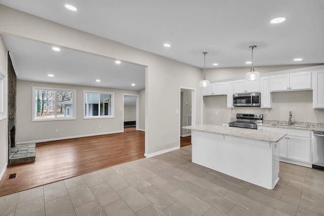 kitchen featuring stainless steel appliances, pendant lighting, white cabinetry, and light stone countertops