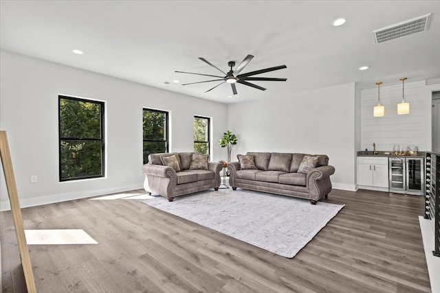 living room with wine cooler, ceiling fan, bar area, and hardwood / wood-style floors