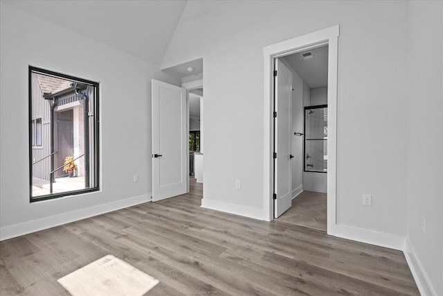 unfurnished bedroom with multiple windows, connected bathroom, light wood-type flooring, and vaulted ceiling