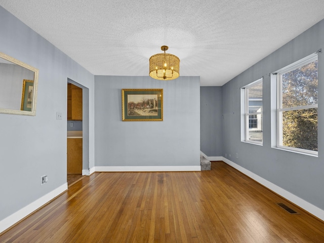 empty room featuring hardwood / wood-style flooring, a textured ceiling, and a chandelier