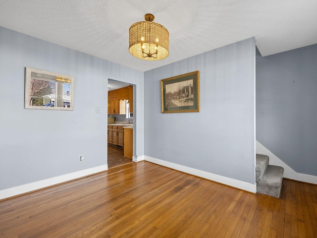 empty room with a textured ceiling, an inviting chandelier, and hardwood / wood-style floors