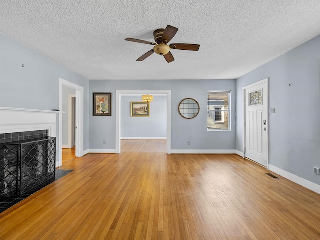 unfurnished living room featuring light hardwood / wood-style floors, a textured ceiling, a tile fireplace, and ceiling fan